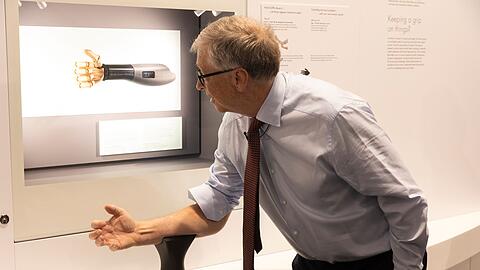 Bill Gates probiert im Deutschen Museum eine Handprothese aus, die sich über die Armmuskeln steuern lässt.