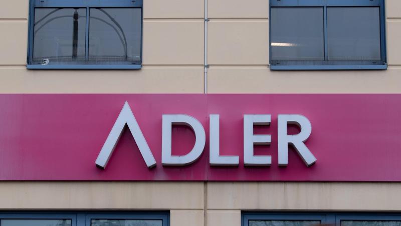 Eine Frau geht an einem Schild des Unternehmens Adler Modemärkte an einem Einkaufszentrum vorbei.