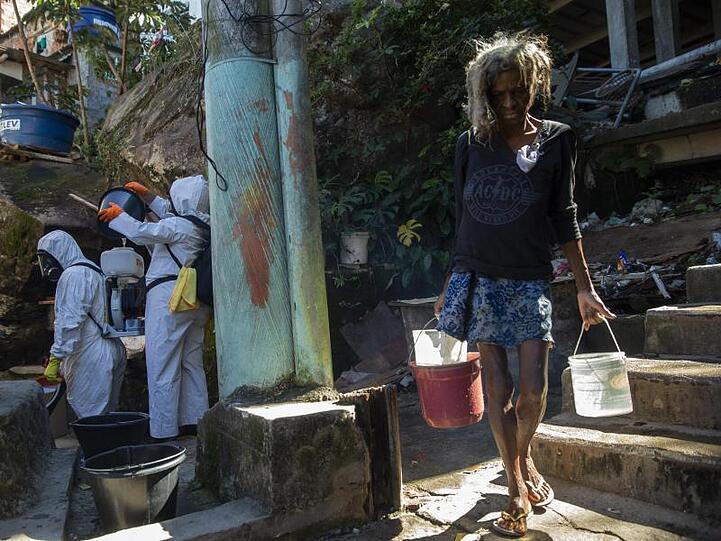 Eine Bewohnerin in einer Favela in Rio de Janeiro holt Wasser, während Freiwillige versuchen das Viertel zu desinfizieren.