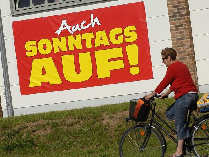 Eine Radfahrerin fährt an einem großen Plakat mit der Aufschrift "Auch Sonntags auf" vorbei. Foto: Stefan Sauer/Archiv