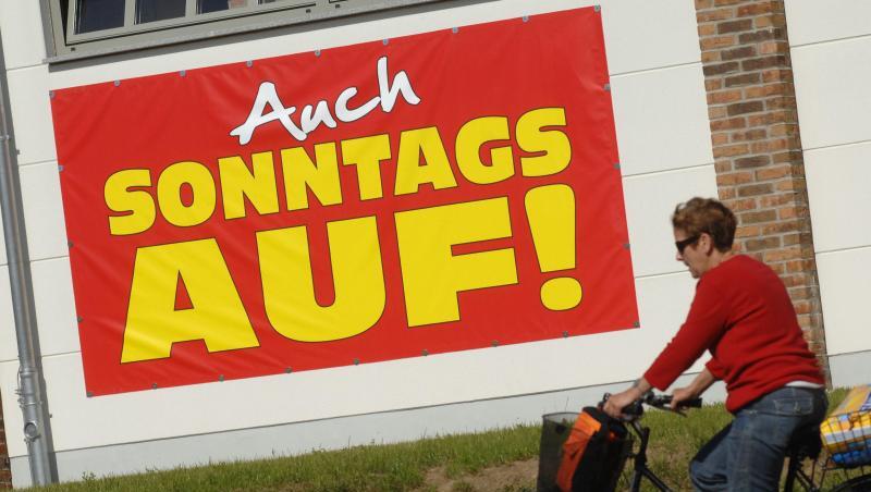 Eine Radfahrerin fährt an einem großen Plakat mit der Aufschrift "Auch Sonntags auf" vorbei. Foto: Stefan Sauer/Archiv Eine Radfahrerin fährt an einem großen Plakat mit der Aufschrift "Auch Sonntags auf" vorbei. Foto: Stefan Sauer/Archiv