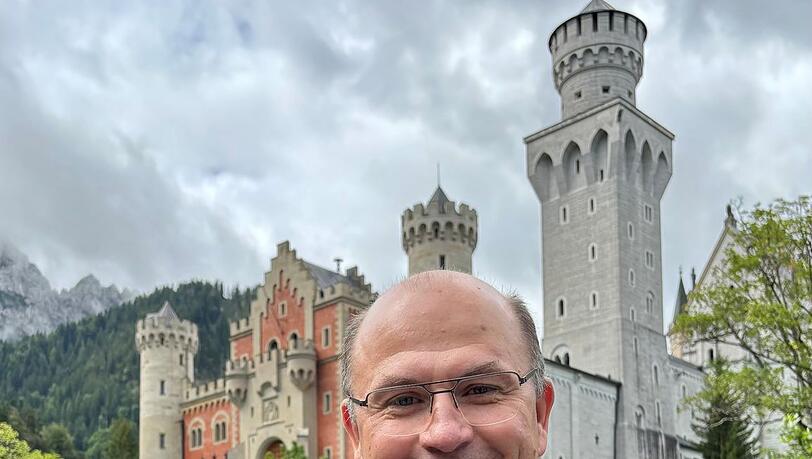 Finanzminister Albert Füracker (CSU) mit dem "Bayern Thaler" in der Hand vor Schloss Neuschwanstein.