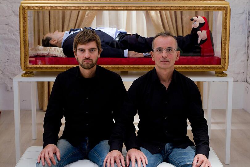 Die beiden Künstler Antonio Garullo and Mario Ottocento posieren vor dem Glassarg mit der Wachsleiche von Silvio Berlusconi.