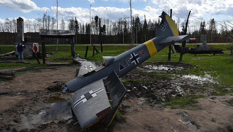 Ein nachempfundenes Flugzeug der deutschen Luftwaffe mit Hakenkreuz steckt auf einem nachgestellten Schlachtfeld im Boden. Ein nachempfundenes Flugzeug der deutschen Luftwaffe mit Hakenkreuz steckt auf einem nachgestellten Schlachtfeld im Boden.