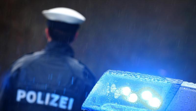 Ein Polizist steht im Regen vor einem Streifenwagen dessen Blaulicht aktiviert ist.