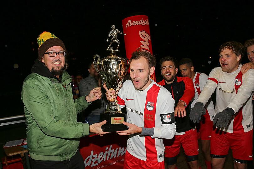 Sebastian Pötsch von der Royal Bavarian League übergibt den Pokal an Fayern-Kapitän Jonas Brachmann.