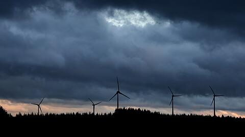 Windräder stehen unter dichten Regenwolken hinter einem Wald.
