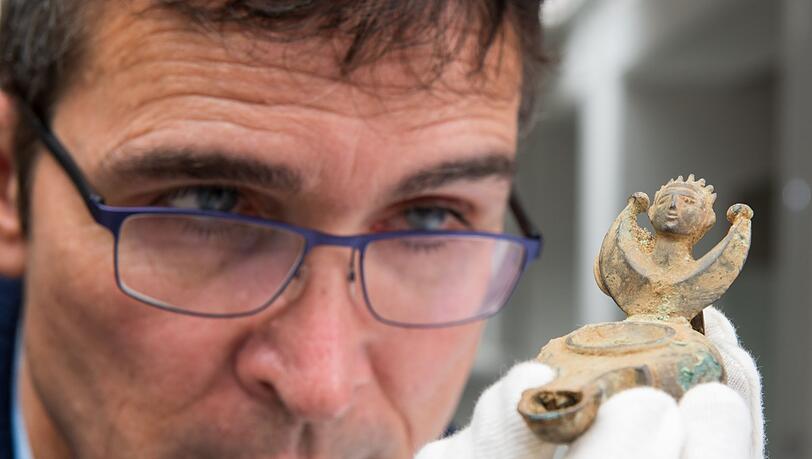 Augsburgs Stadtarchäologe Sebastian Gairhos betrachtet eine antike Öllampe, die vor wenigen Jahren in Bayerns ältestem Römerlager entdeckt wurde. (Archivbild)