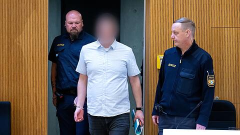 Einer von zwei wegen Mordes angeklagten Männern (M) wird in den Gerichtssaal geführt.