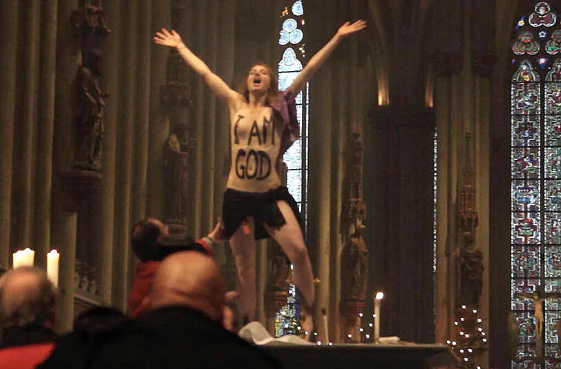 Eine Femen-Aktivistin posiert am 25.12.2013 mit bemaltem Oberkörper «I am God» während der Weihnachtsmesse im Kölner Dom auf dem Altar. Am 03.12.2014 steht die Aktivistin vor Gericht.