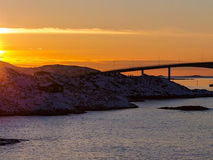 Die Sonne geht hinter der Sommaroy-Brücke unter, die die Inseln Kvaloya und Sommaroy verbindet.