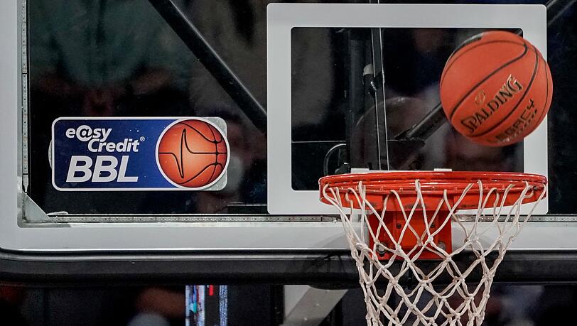 Ein Ball fliegt auf den Korb zu, an dem ein Logo der Basketball-Bundesliga klebt.
