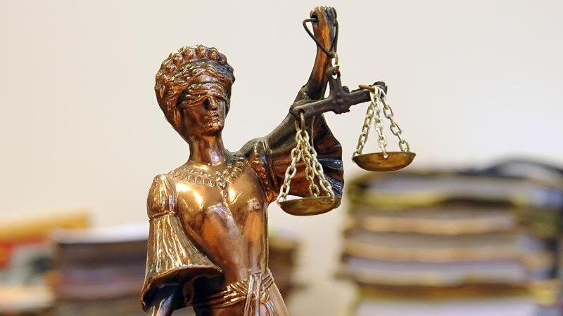 Eine goldfarbene Justitia-Figur steht vor Aktenbergen. Foto: Britta Pedersen/Archiv