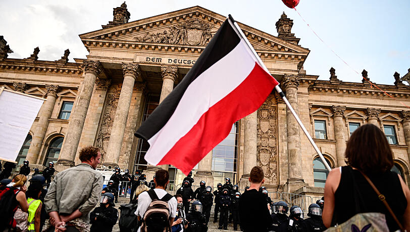 Ein Bild vom vergangenen Samstag: Teilnehmer einer Kundgebung gegen die Corona-Maßnahmen stehen vor dem Reichstag, ein Teilnehmer hält eine Reichsflagge.