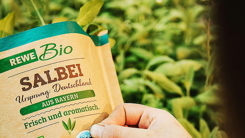 Eine Hand hält eine Salbeiverpackung mit dem Bayerischen Bio-Siegel. Eine Hand hält eine Salbeiverpackung mit dem Bayerischen Bio-Siegel.