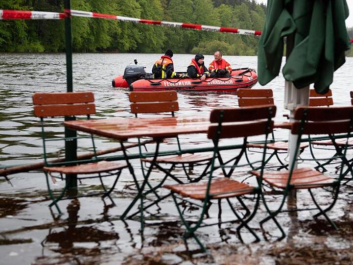 Feuerwehrmänner fahren mit einem Boot über den Deininger Weiher, der durch den starken Regen einen hohen Wasserstand hat und bereits einen Biergarten überflutet hat. Foto: Sven Hoppe