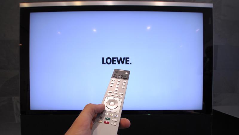 Mit einer Fernbedienung wird im Showroom der Loewe-Firmenzentrale ein Flachbildfernseher bedient. Foto: David-Wolfgang Ebener/dpa/Archivbild