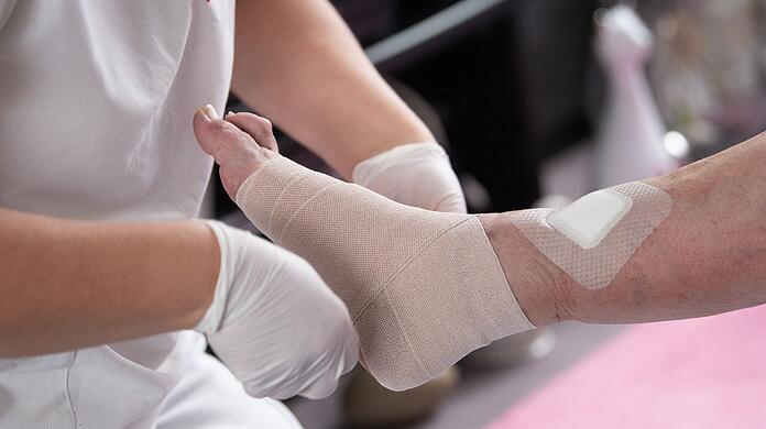 Eine Pflegefachkraft legt in der ambulanten Pflege einen Kompressionsverband an.