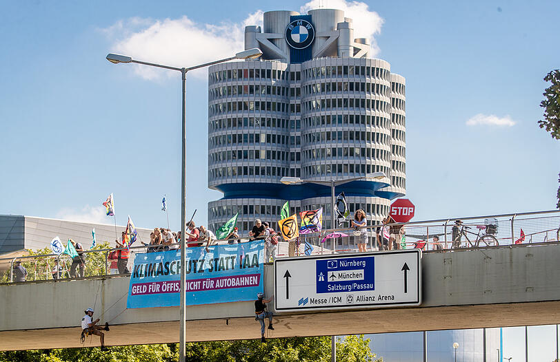 Während im Hintergrund die BMW-Welt zu sehen ist, seilen sich Klimaaktivisten der Extinction Rebellion München über der Fahrbahn ab.