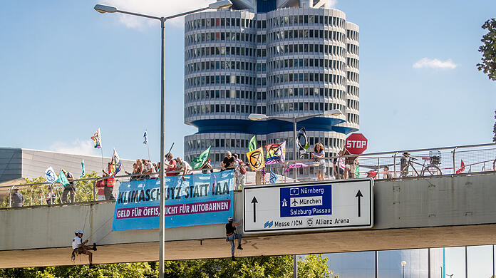 Während im Hintergrund die BMW-Welt zu sehen ist, seilen sich Klimaaktivisten der "Extinction Rebellion" in München über der Fahrbahn ab.