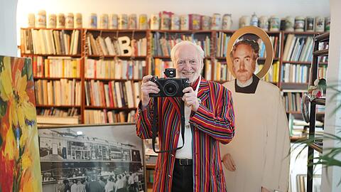 Wolfgang Roucka in seiner Wohnung in Schwabing. Hinter ihm zu sehen ist ein Pappaufsteller, den seine Mitarbeiter für ihn gebastelt haben.