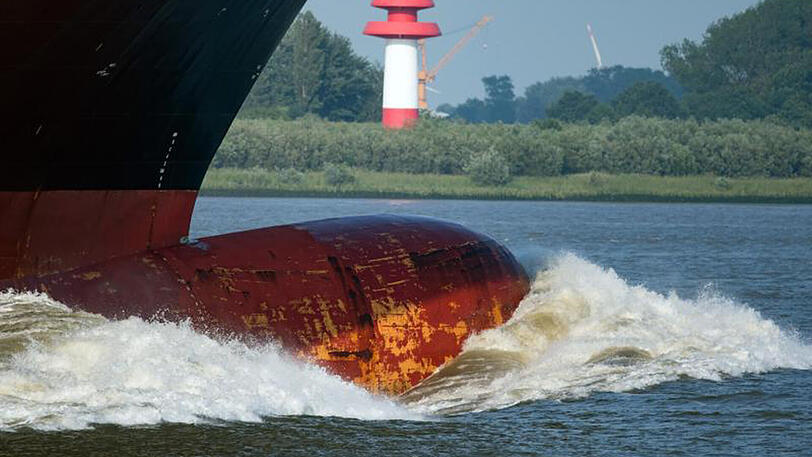 Der Bug eines Containerfrachters schiebt vor der Hamburger Hafeneinfahrt eine große Welle vor sich her.