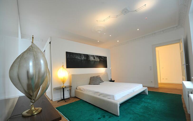 Das Schlafzimmer liegt wie alle Privaträume der 256-Quadratmeter-Wohnung im Altbau-Teil des Gebäudes. Hinterm Bett ist ein begehbarer Kleiderschrank, oben ist Stuck an der Decke.
