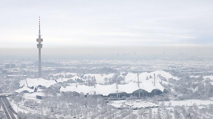 Der schneebedeckte Olympiapark mit dem Olympiaturm ist von einem Hochhaus zu sehen.