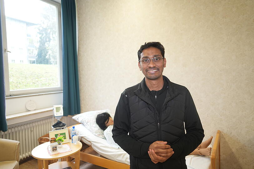 Fortzubildender Mohamed Rafi Esmael. Der geb&uuml;rtige Inder steht vor einer der lebensnahen und menschenschweren Pflegepuppen.