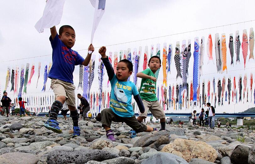 Kleine Jungs spielen am Flussufer in Sagamihara, einem Vorort von Tokyo, in Erwartung des offiziellen Kindertages in Japan am 5.Mai. Aufgehängte Fähnchen, die sogenannten 'Koinobori'symbolisieren die elterlichen Wünsche auf Kraft und Stärke für ihre Kinder.