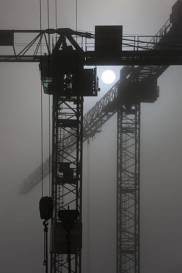 Nebulös: Die Metallskelette der Baukräne stechen als Silhouette in den Himmel.
