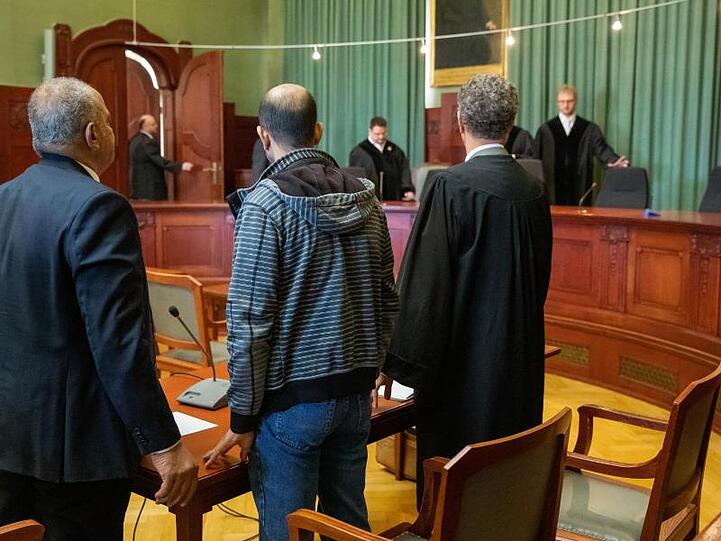 Ein wegen Mordes angeklagter Marokkaner (M) steht zu Verhandlungsbeginn im Sitzungssaal im Landgericht Bayreuth zwischen seinem Anwalt (r) und einem Übersetzer. Foto: Daniel Karmann