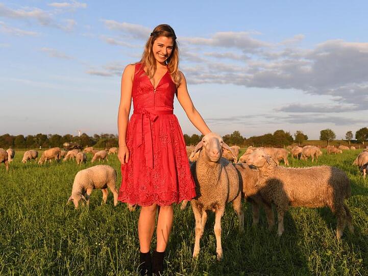 Das Wiesn-Playmate 2019, Stella Stegmann, steht in der Abendsonne auf einer Wiese zwischen Schafen. Foto: Felix Hörhager/Archivbild