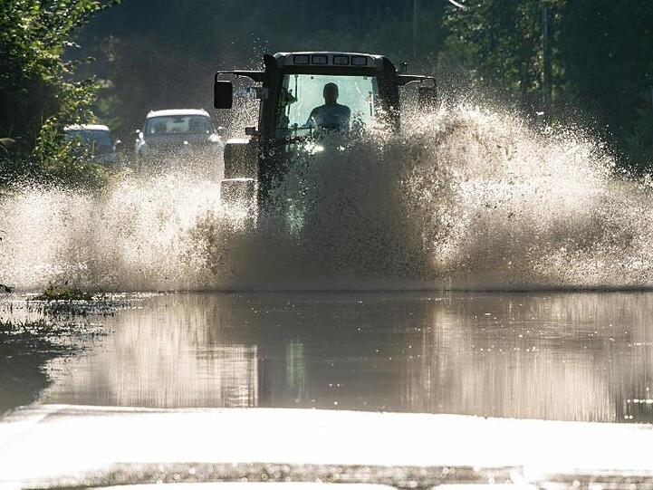 Ein Traktor fährt über eine Straße, die nach den starken Regenfälle unter Wasser steht. Foto: Peter Kneffel/dpa