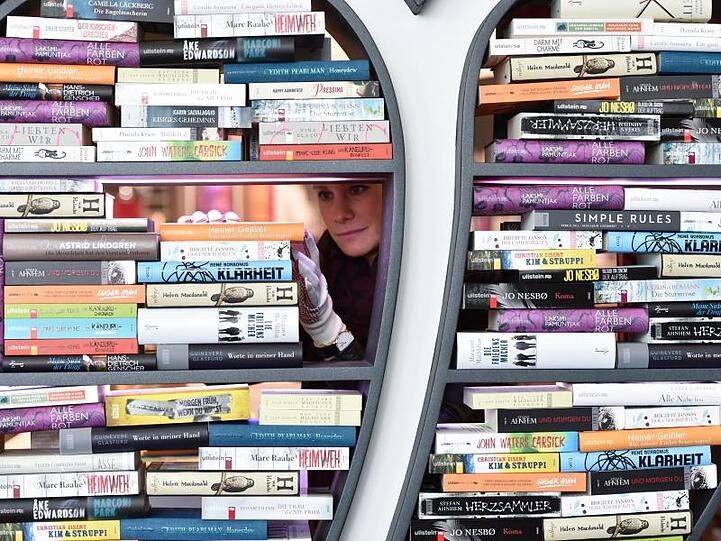 Eine Frau dekoriert ein Regal mit Büchern. Foto: Arne Dedert/dpa