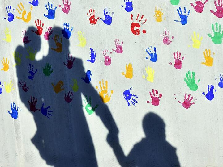 Schatten auf eine mit bunten Handabdrücken bemalte Wand einer Kindertagesstätte. Foto: Peter Kneffel/dpa/Archivbild