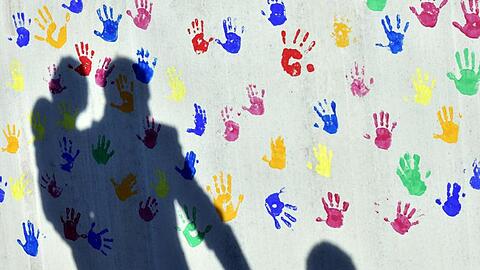 Schatten auf eine mit bunten Handabdrücken bemalte Wand einer Kindertagesstätte. Foto: Peter Kneffel/dpa/Archivbild