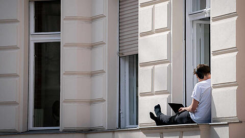 Ein Mann hat sein Homeoffice auf die sonnige Fensterbank seiner Wohnung verlegt.