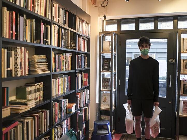 Tom, Filialleiter der Broadway-Buchhandlung im Broadway Market, hält zwei Säcke mit Büchern in der Hand, die von den Kunden abgeholt werden müssen.