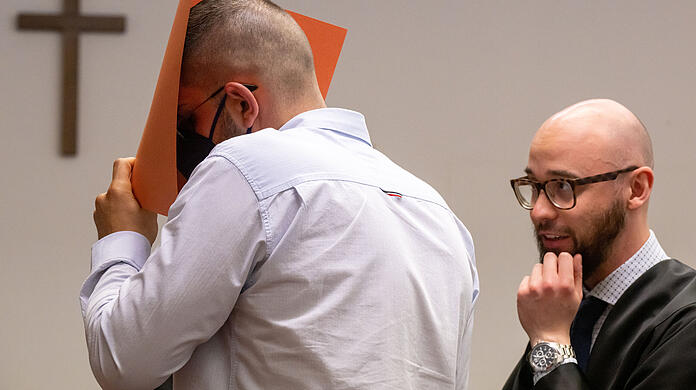 Der Angeklagte verdeckt im Gerichtssaal sein Gesicht mit einem Aktendeckel. Rechts steht sein Anwalt Deniz Aydin. Der Mann soll sich an einer schlafenden Frau vergangen haben, die er als Fahrer in seinem Taxi transportierte.