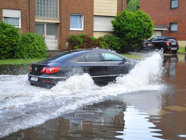 Ein Auto fährt nach heftigen Regenfällen durch eine überflutete Straße in Mönchengladbach.