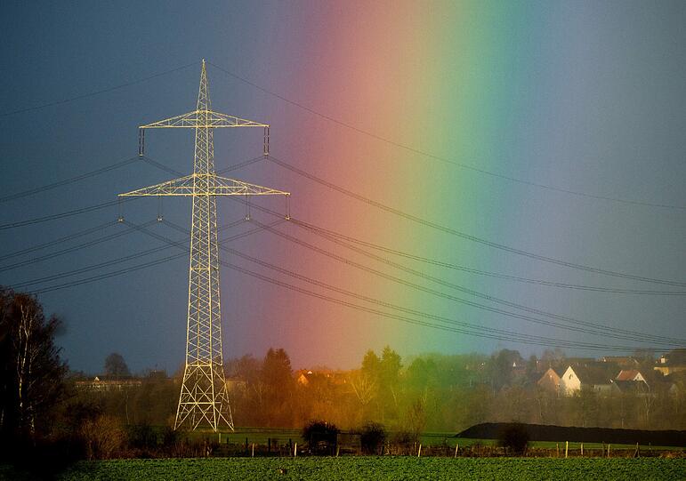 Ein Regenbogen spannt sich am 29.03.2015 bei stürmischen Wetter über Felder mit einer Hochspannungleitung bei Sehnde in der Region Hannover (Niedersachsen).
