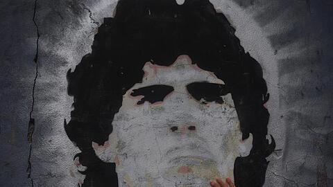 Ein Fan des Fußballclubs Boca Juniors legt die Hand auf ein Wandgemälde von Diego Maradona.