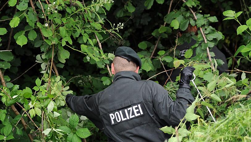 Ein Polizist durchsucht das Gebüsch (Symbolbild). Ein Polizist durchsucht das Gebüsch (Symbolbild).