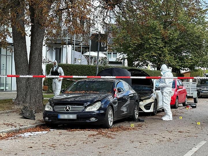 Beamte der Spurensicherung sind neben zwei ausgebrannten Autos im Einsatz.