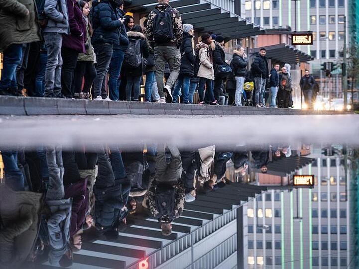 Zahlreiche Pendler warten in Frankfurt an einer Haltestelle.