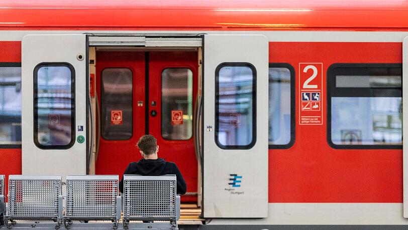 Ein Mann sitzt an einem Bahnhof vor einem Regionalzug auf der Bank.