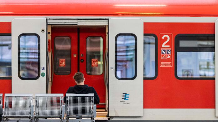 Ein Mann sitzt an einem Bahnhof vor einem Regionalzug auf der Bank.