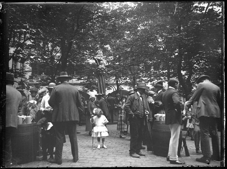 1925 sind im Hof des Hofbräuhauses die Gäste in Gespräche vertieft. Nur das Mädchen in dem weißen Kleidchen und der kleine Bub links scheinen sich arg zu langweilen zwischen all den behuteten Männern.