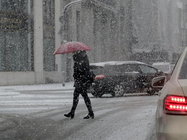 Ein Frau mit Schirm geht im Schneetreiben über eine Straße in Köln.